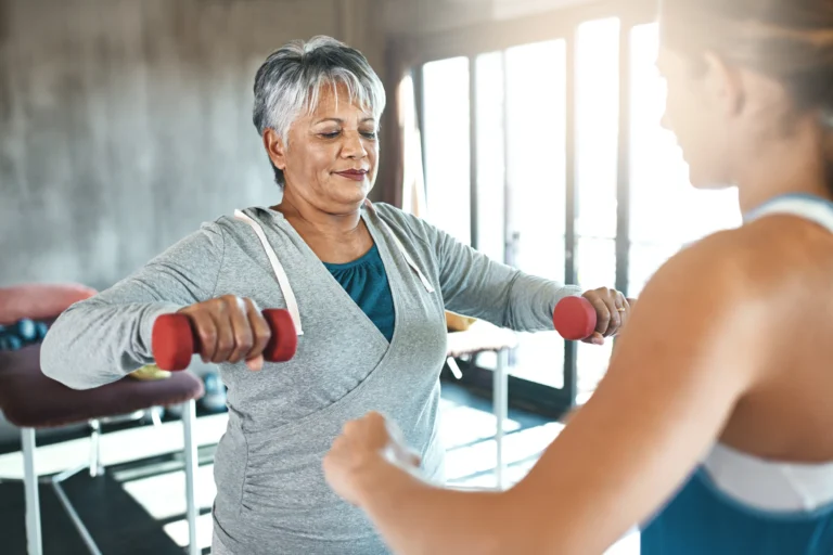 Older woman lifting dumbbells with a personal trainer