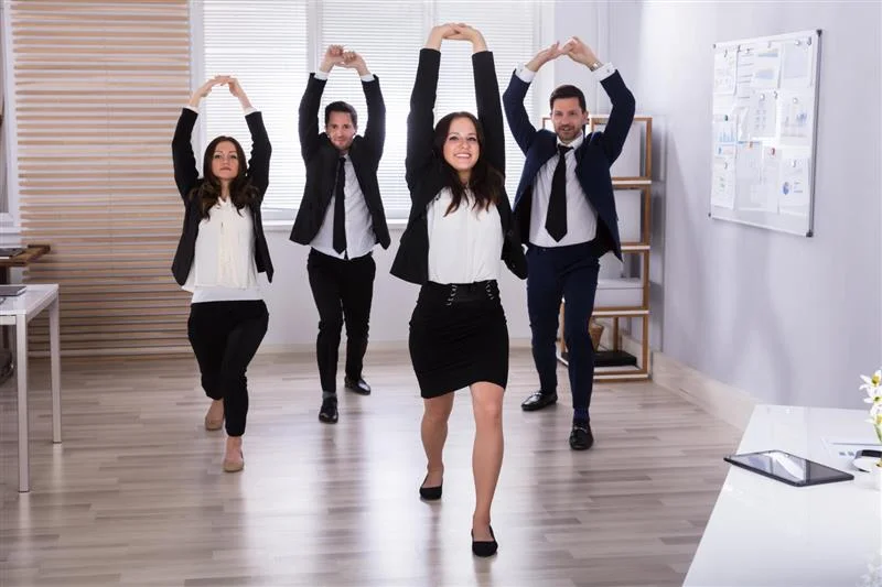 Employees participating in a workplace stretching session in a modern office, part of a corporate wellness program in Newport Beach