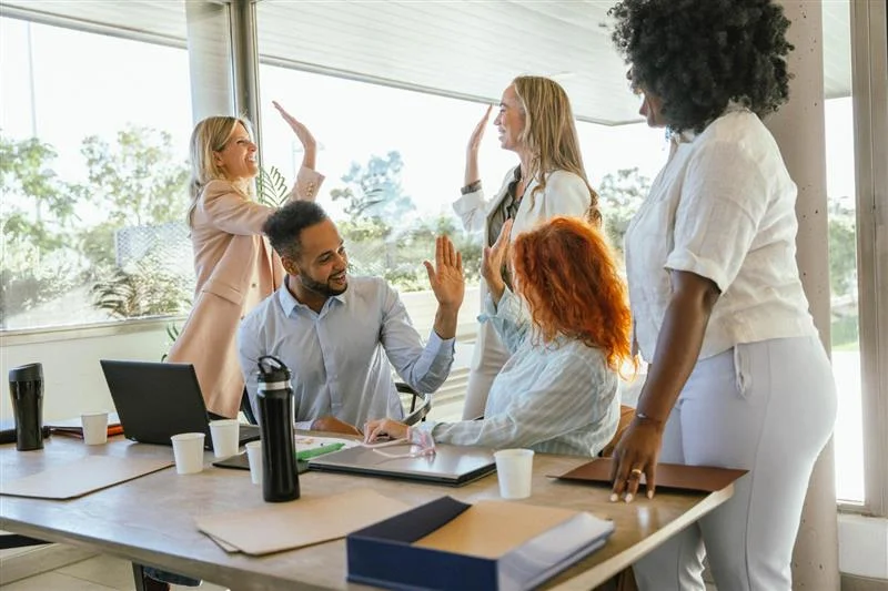 Business team celebrating success in a modern office, representing increased morale and engagement from workplace wellness programs