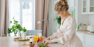 Woman preparing a healthy salad in a bright coastal kitchen, representing balanced nutrition and sustainable healthy eating for women