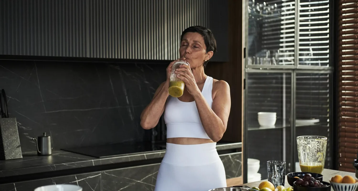 Woman over 35 drinking smoothie after workout in kitchen